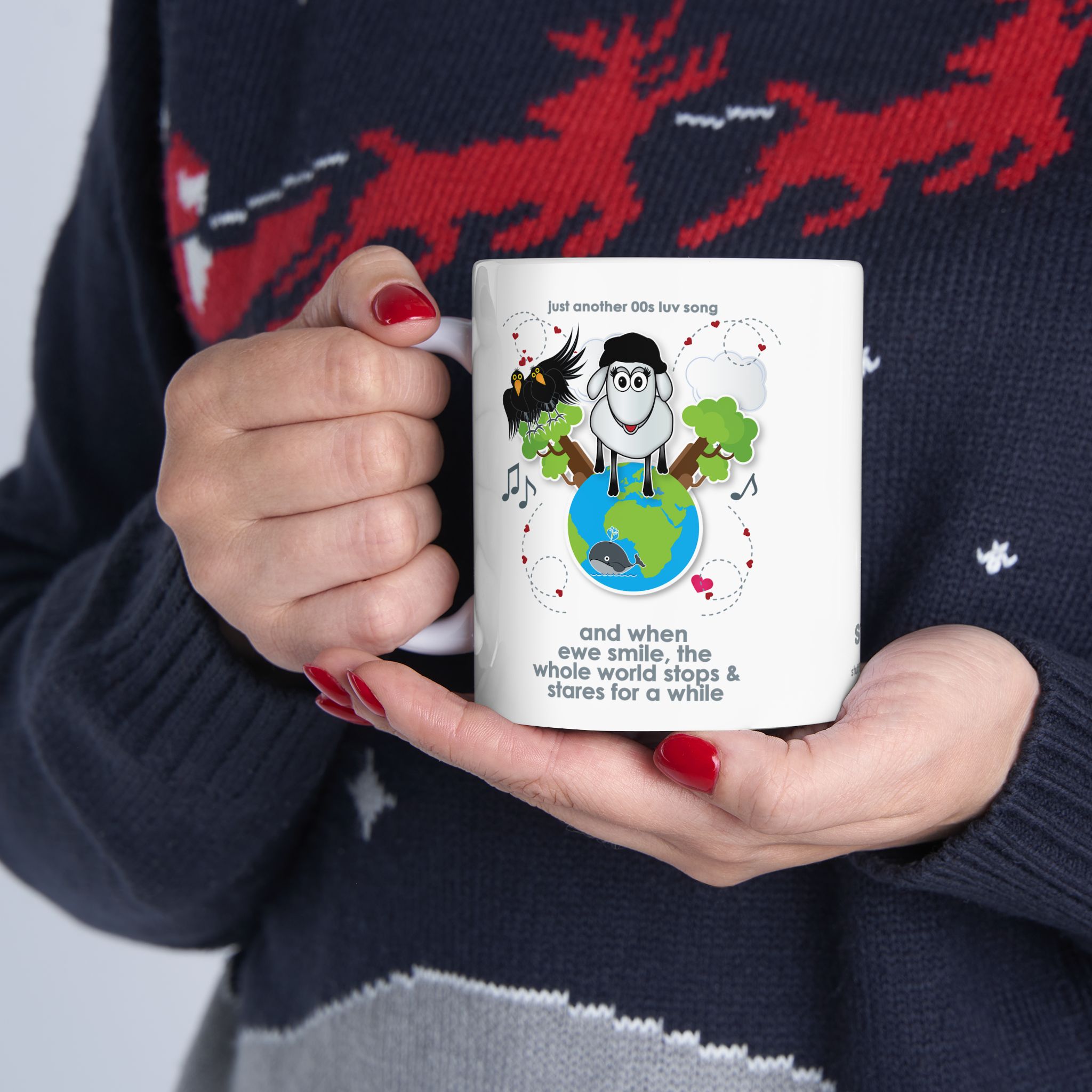 When Ewe Smile Love Song Mug (11oz, 15oz) 9 White ceramic mug printed with a cartoon sheep and some crows on a globe, text reads "and when ewe smile the whole world stops & stares for a while" held by woman in Christmas jersey