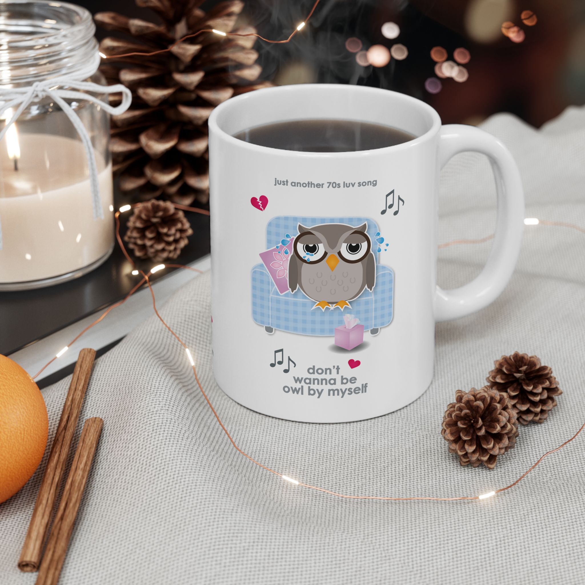 Owl By Myself Love Song Mug (11oz, 15oz) 4 White ceramic Owl By Myself Mug featuring a cartoon owl, crying on a blue chair with a box of tissues, text reads "don't wanna be owl by myself" on a table with pine cones, cinnamon sticks, a candle, an orange and fairy lights