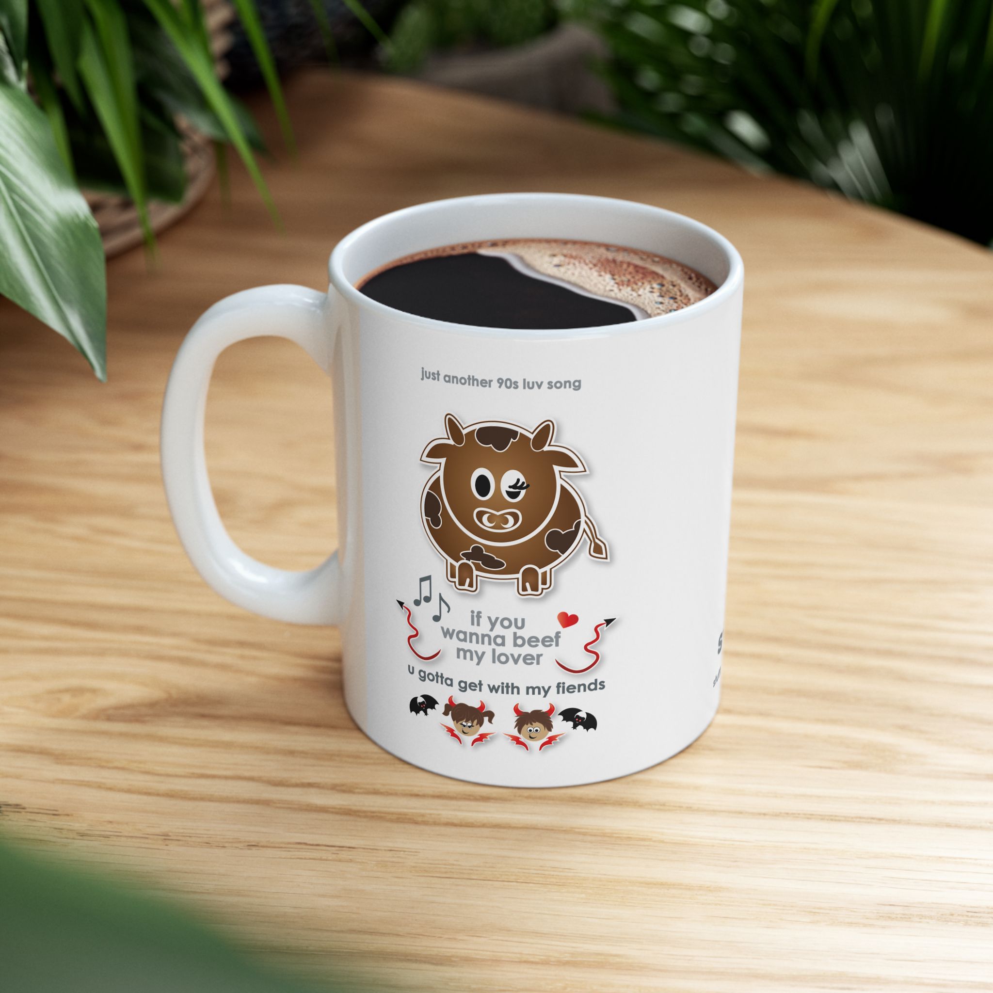 Beef My Lover Love Song Mug (11oz, 15oz) 7 White ceramic Beef my Lover love song mug featuring a cartoon cow, an angel and a fiend, text reads "if you wanna beef my lover, u gotta get with my fiends" on wooden table