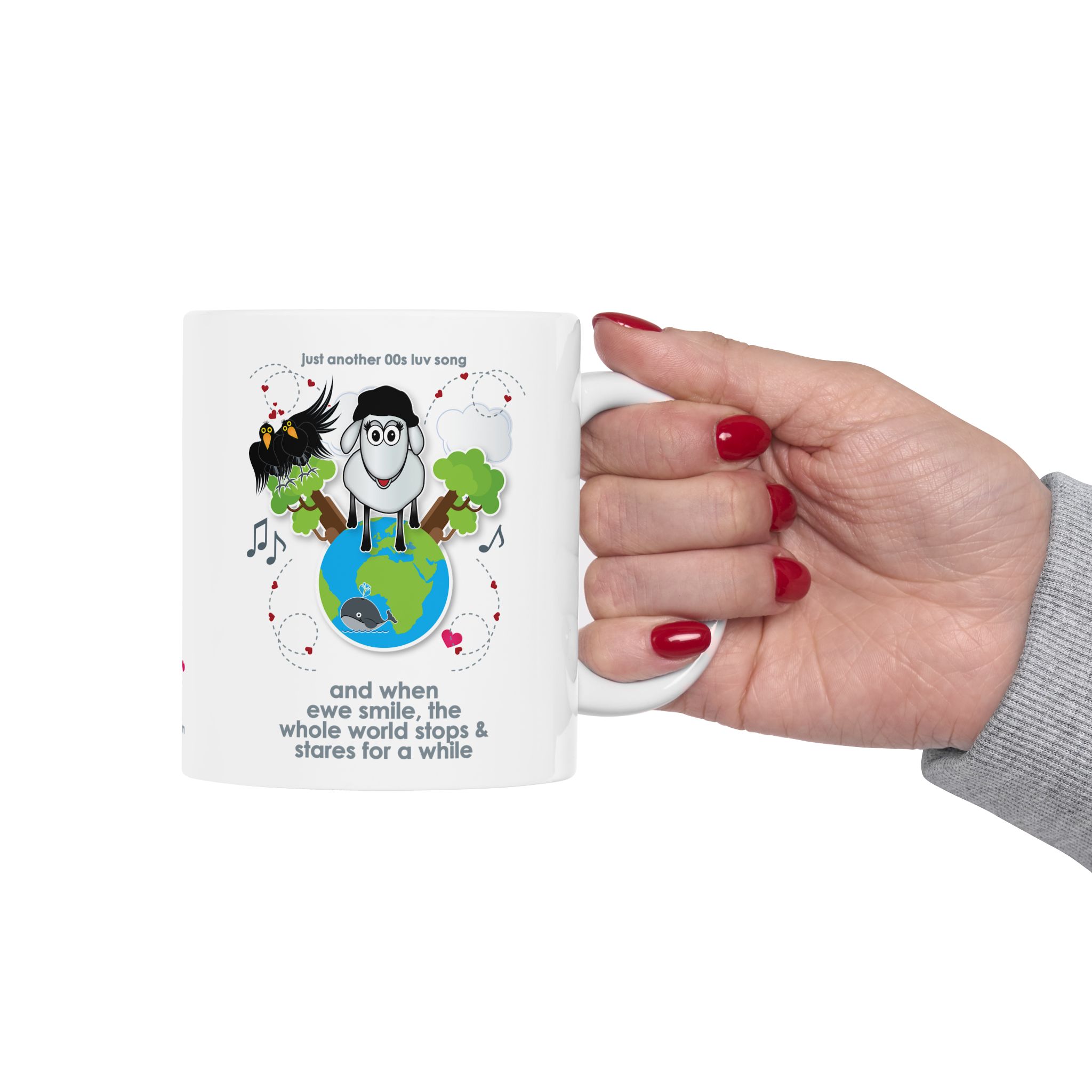 When Ewe Smile Love Song Mug (11oz, 15oz) 10 White ceramic mug printed with a cartoon sheep and some crows on a globe, text reads "and when ewe smile the whole world stops & stares for a while" being held by woman's hand with red nail polish