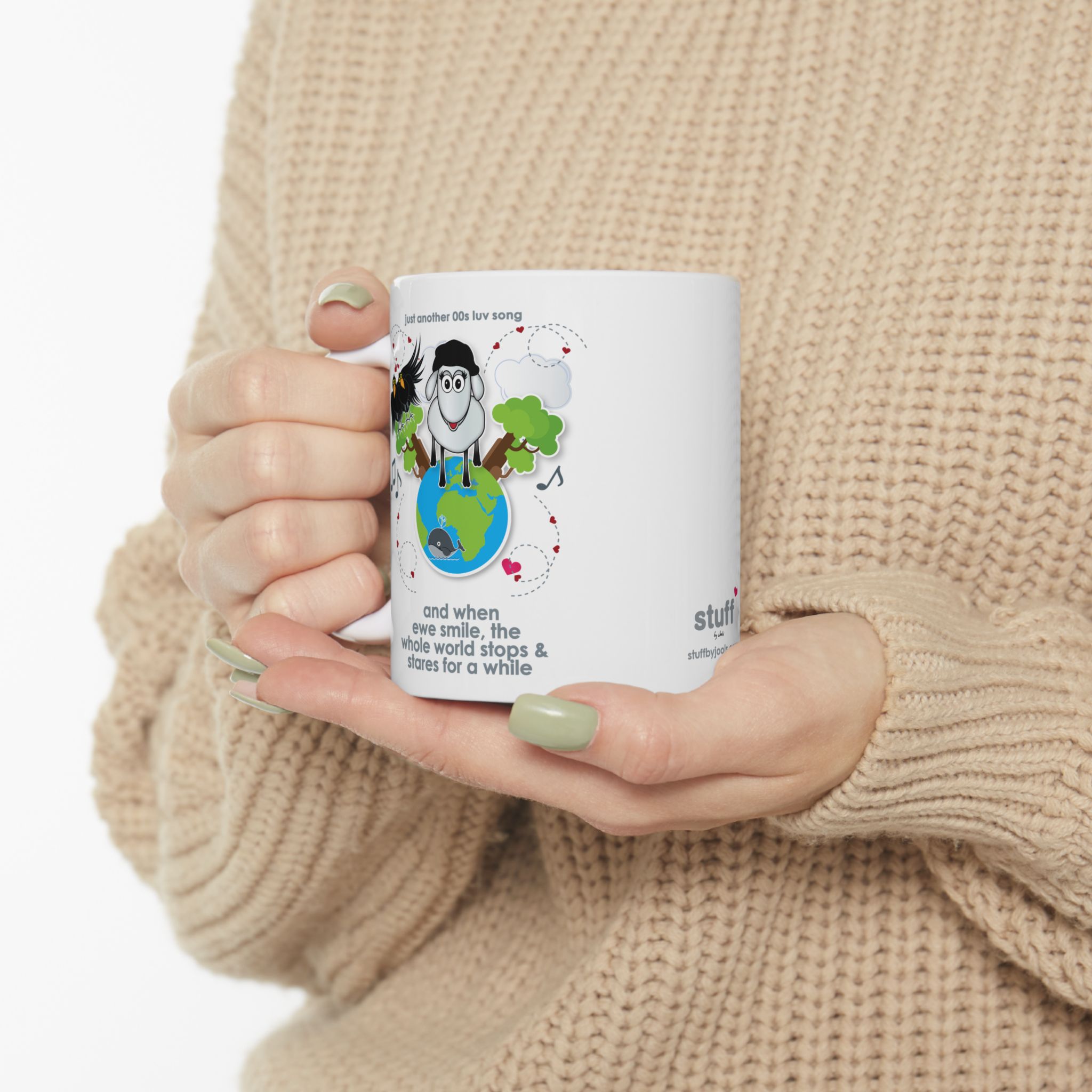 When Ewe Smile Love Song Mug (11oz, 15oz) 8 White ceramic mug printed with a cartoon sheep and some crows on a globe, text reads "and when ewe smile the whole world stops & stares for a while" held by woman in camel-coloured jersey