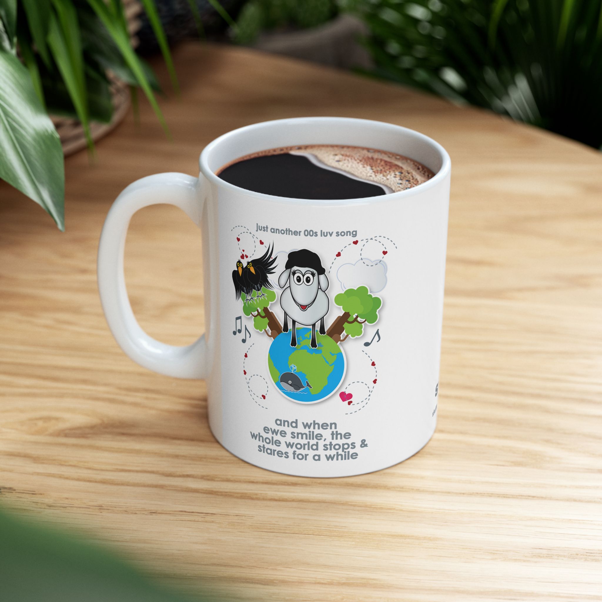 When Ewe Smile Love Song Mug (11oz, 15oz) 7 White ceramic mug printed with a cartoon sheep and some crows on a globe, text reads "and when ewe smile the whole world stops & stares for a while" on wooden table