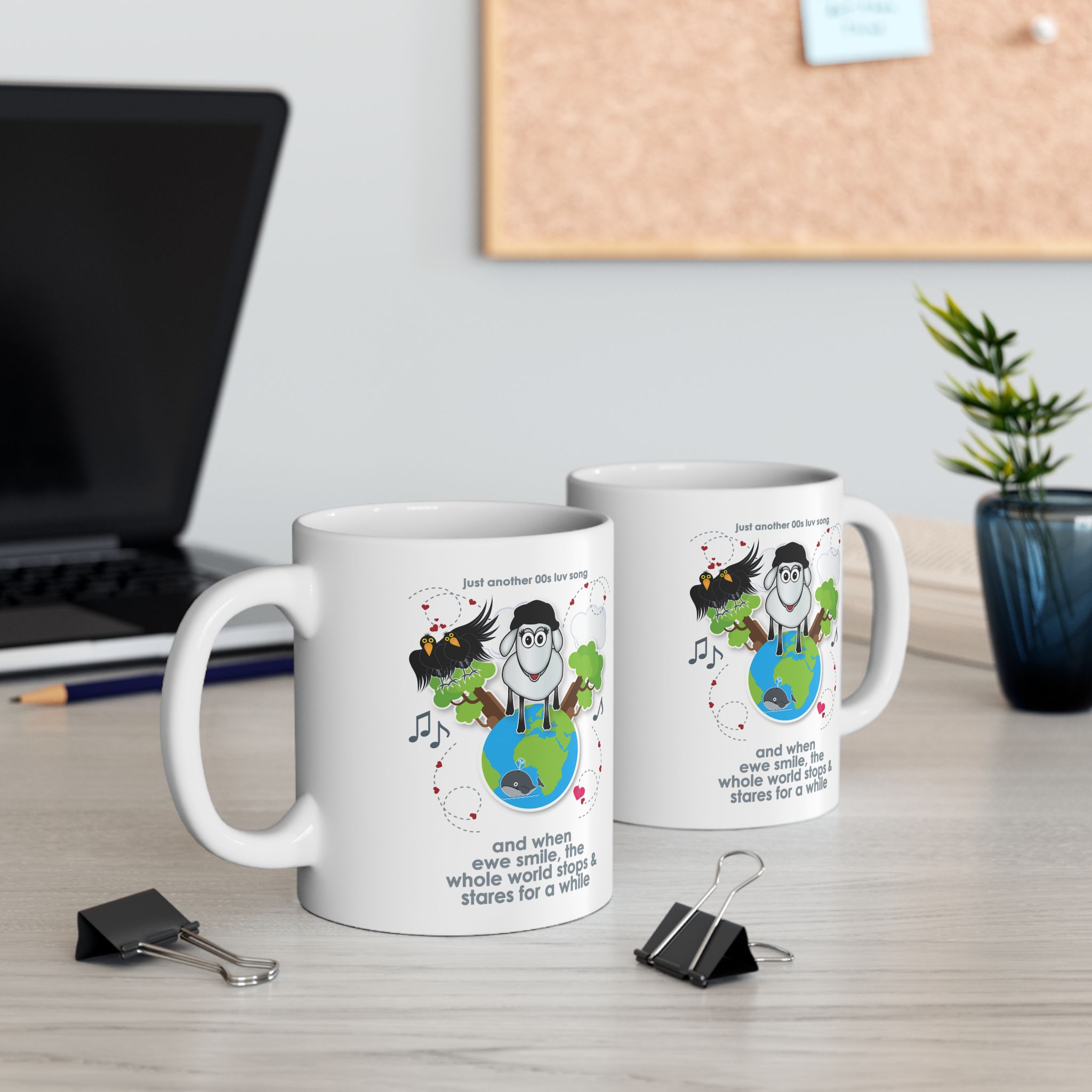 When Ewe Smile Love Song Mug (11oz, 15oz) 5 two white ceramic mugs printed with a cartoon sheep and some crows on a globe, text reads "and when ewe smile the whole world stops & stares for a while" on a desk with a laptop and pot plant